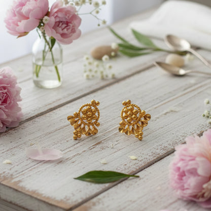 Gold plated earrings on a wooden surface with pink flowers and spoons in the background