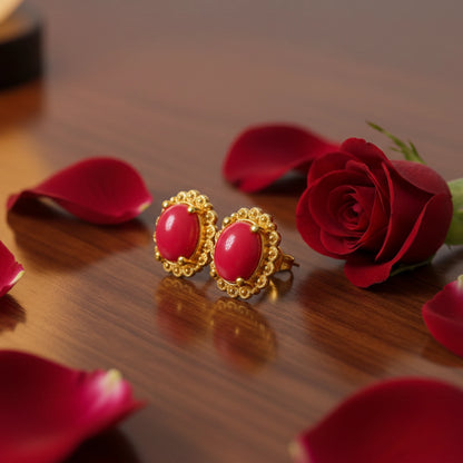 Gold plated earrings with oval red stones on a wooden surface with red roses and petals.