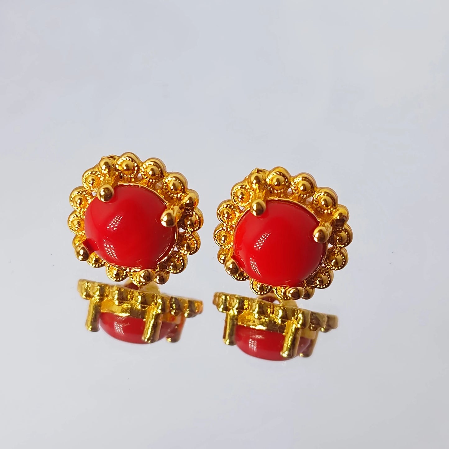 Pair of gold plated earrings with round red stones on a light gray background