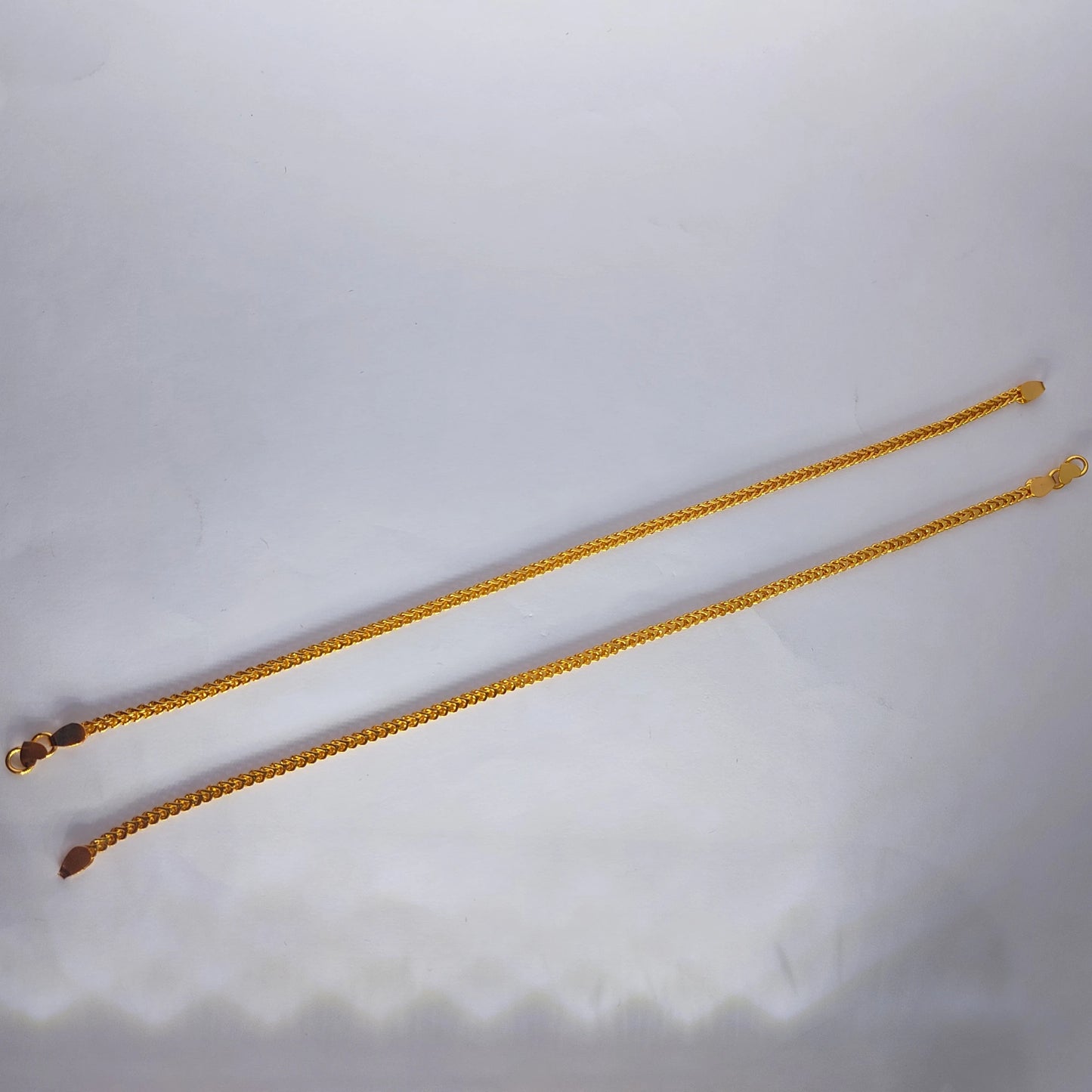 Gold plated anklets on a light gray background