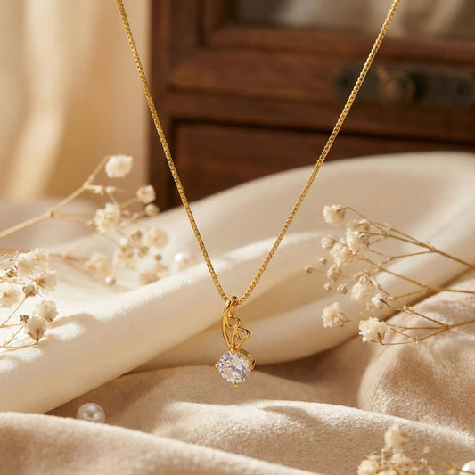 Gold plated neckchain with a diamond pendant on a soft beige surface with dried flowers.