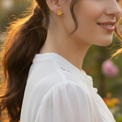 Woman wearing gold plated flower earrings with a blurred natural background