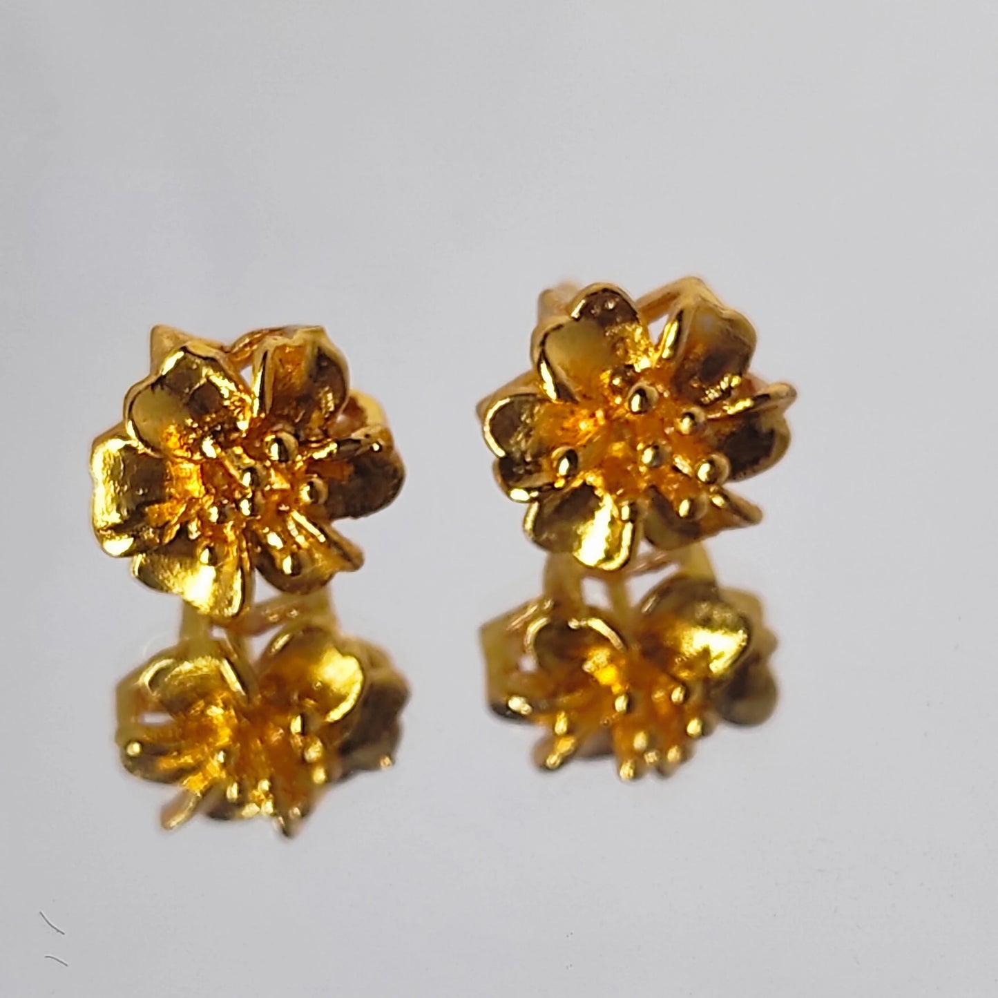 Pair of gold plated flower-shaped earrings on a light gray background