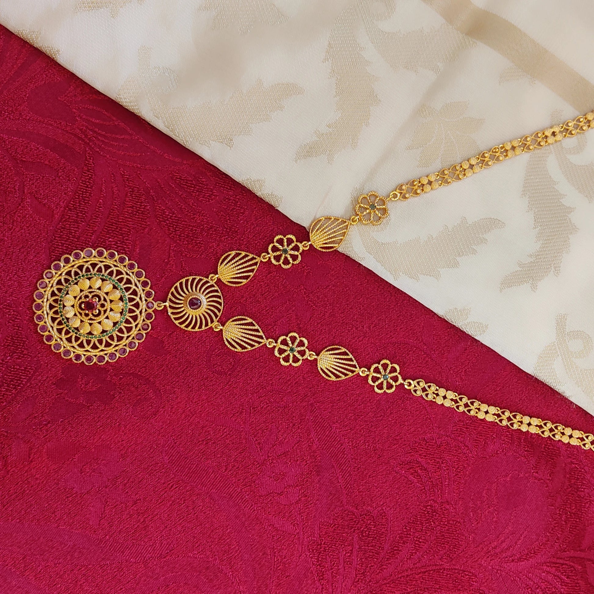 Gold plated long necklace with floral mandala pendant on a red and beige fabric background