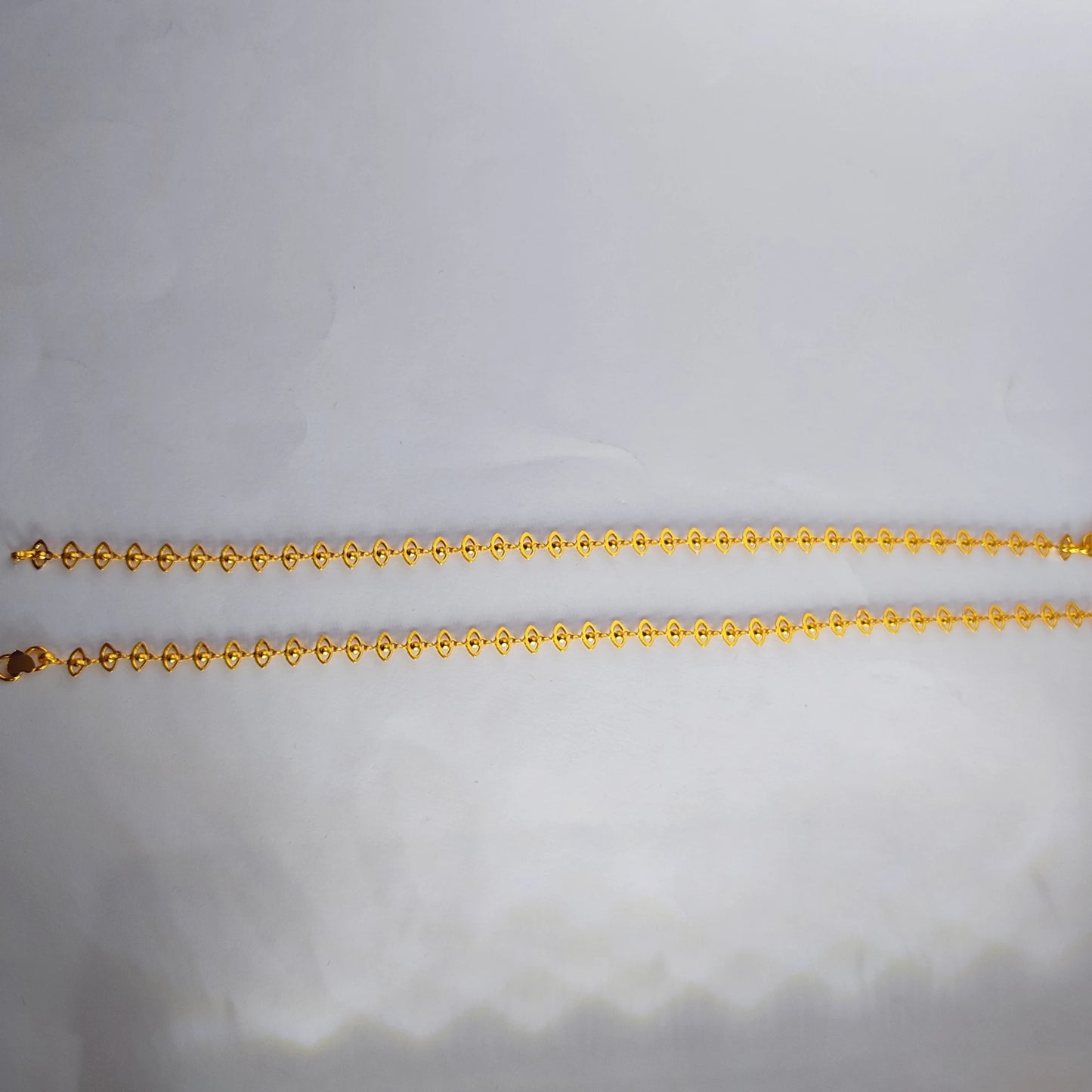 Gold plated delicate lace design anklets on a light gray background