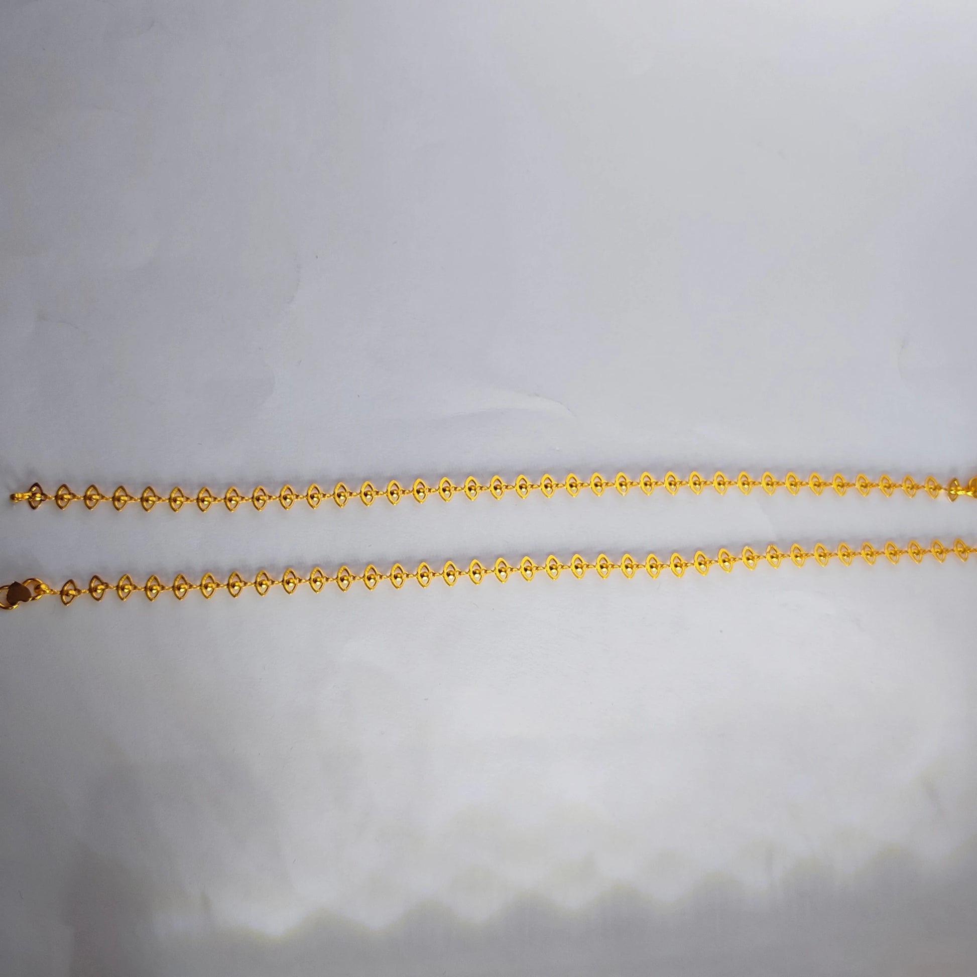 Gold plated delicate lace design anklets on a light gray background