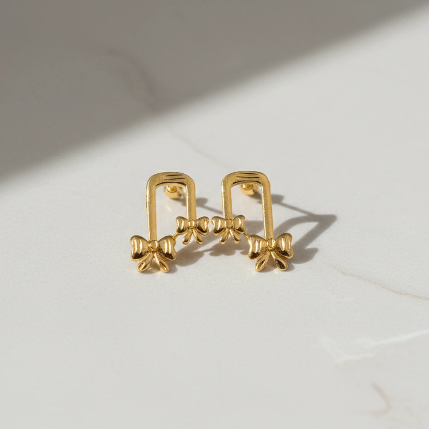 Gold plated ribbon bow-shaped earrings on a light background