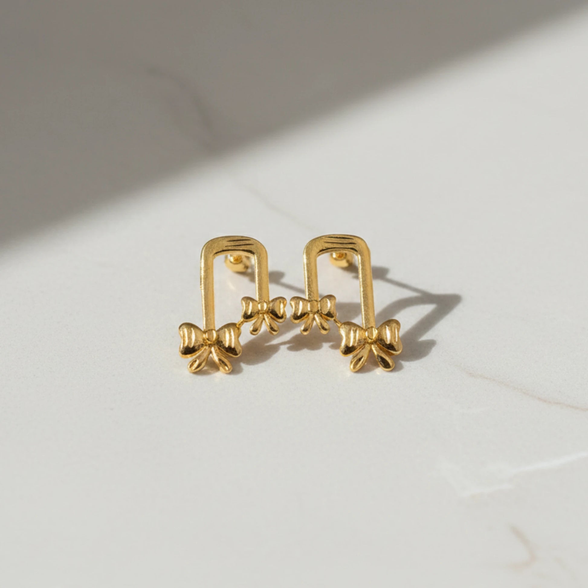 Gold plated ribbon bow-shaped earrings on a light background