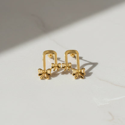 Gold plated ribbon bow-shaped earrings on a light background