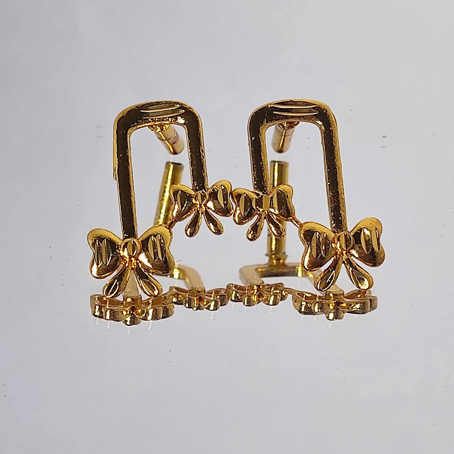 Gold plated ribbon bow-shaped earrings on a light gray background