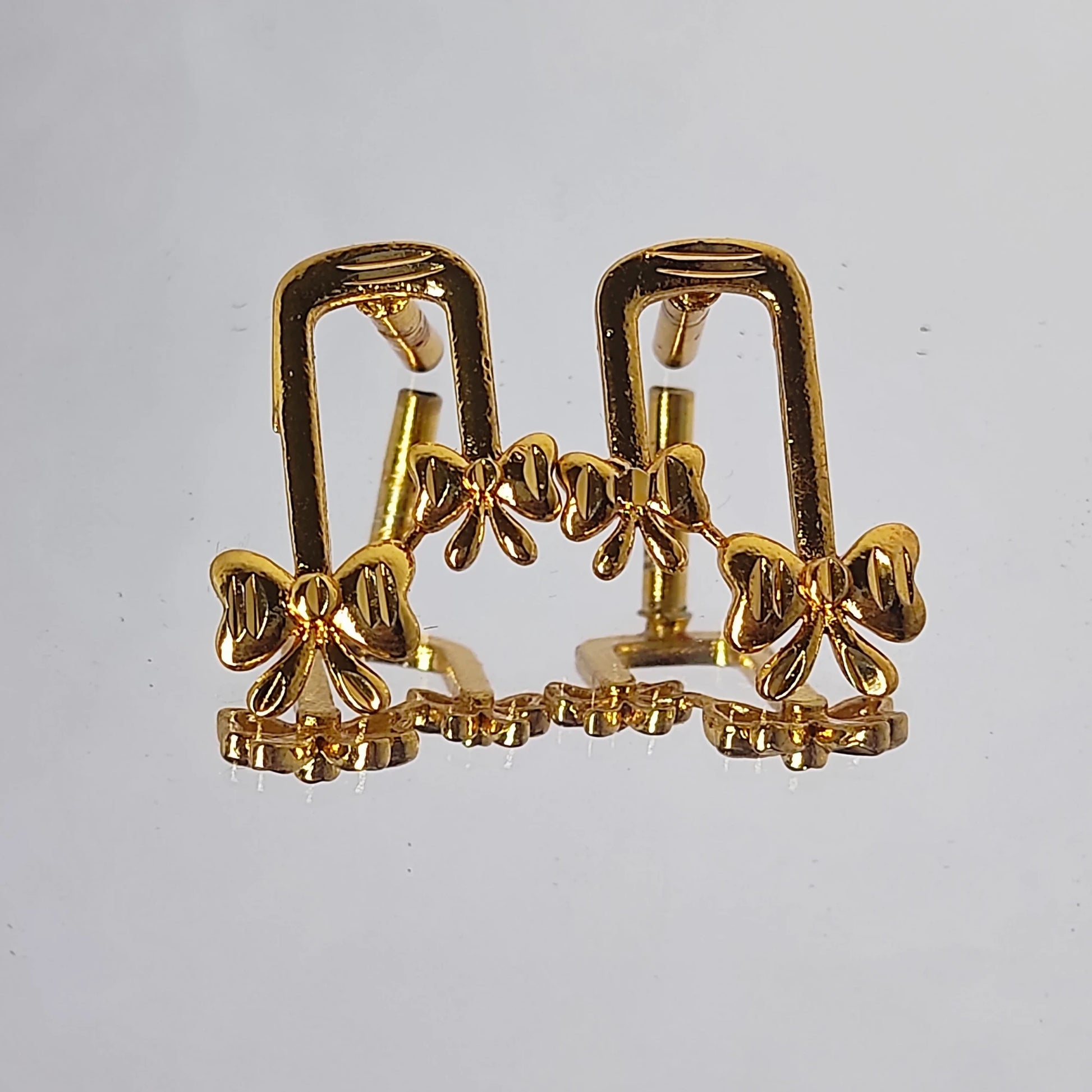 Gold plated ribbon bow-shaped earrings on a light gray background