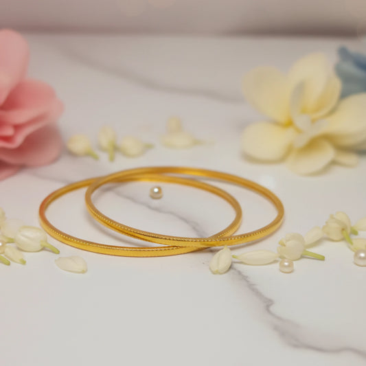 Gold plated minimalist daily wear sleek bangles with pearls on a marble surface with flowers
