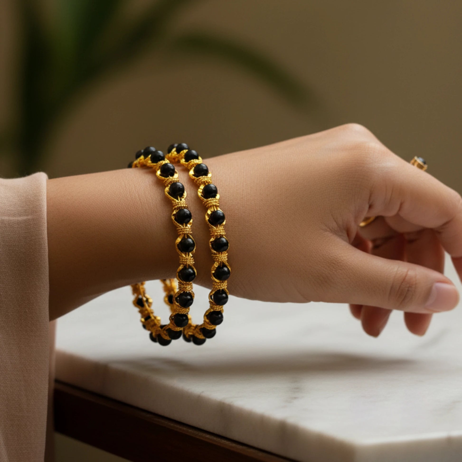 Hand wearing two gold plated karimani/ black beaded bangles on a neutral background