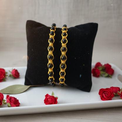 Pair of black bangles in karimani or black beaded on a black pillow with red roses around.