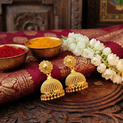 Gold plated Jimikki/jhumka earrings on a decorative surface with flowers and powders.