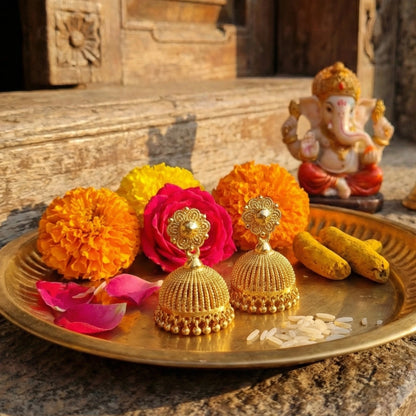 Decorative tray with gold plated Jimikki/Jhumkas earrings, flowers, and a small statue on a stone surface.