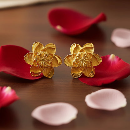 Gold plated floral earrings on red and pink petals with a blurred background