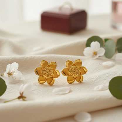 Gold plated flower-shaped earrings on a white fabric background with flowers and leaves.