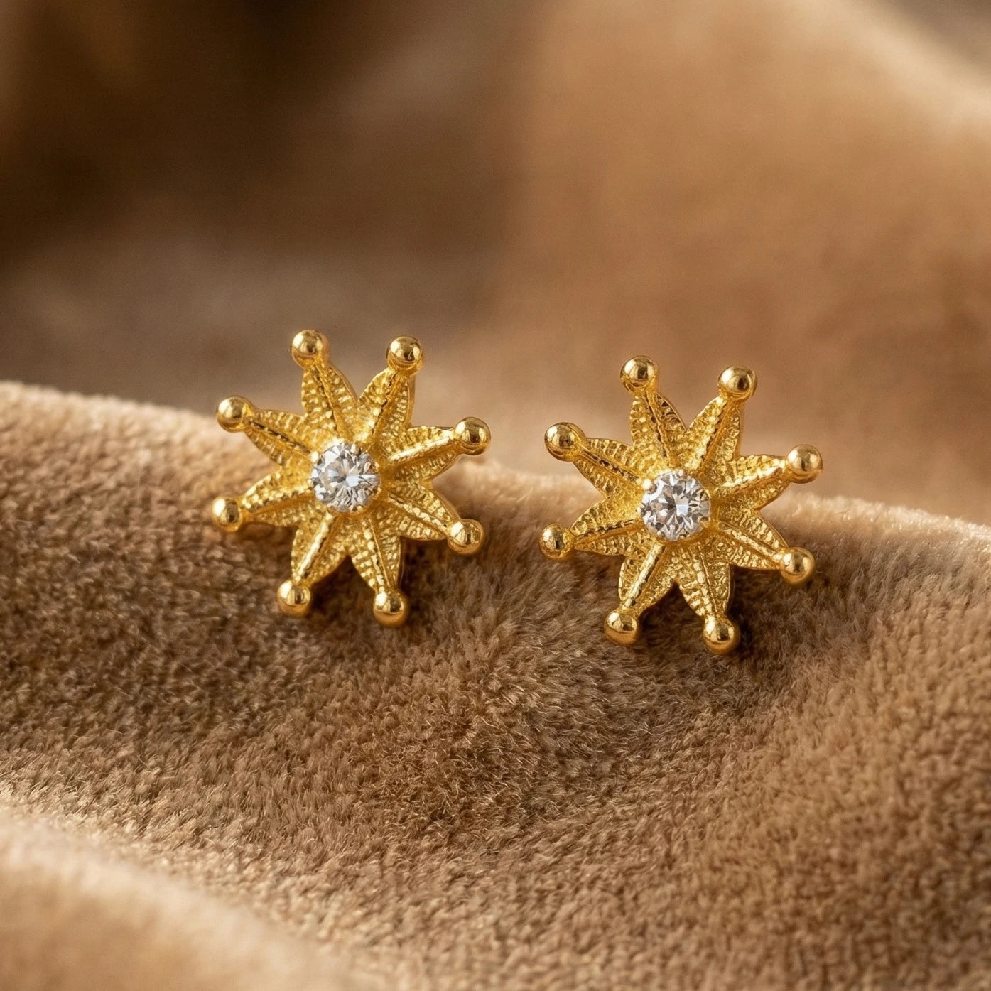 Gold plated star-shaped earrings with a central gemstone on a brown fabric background
