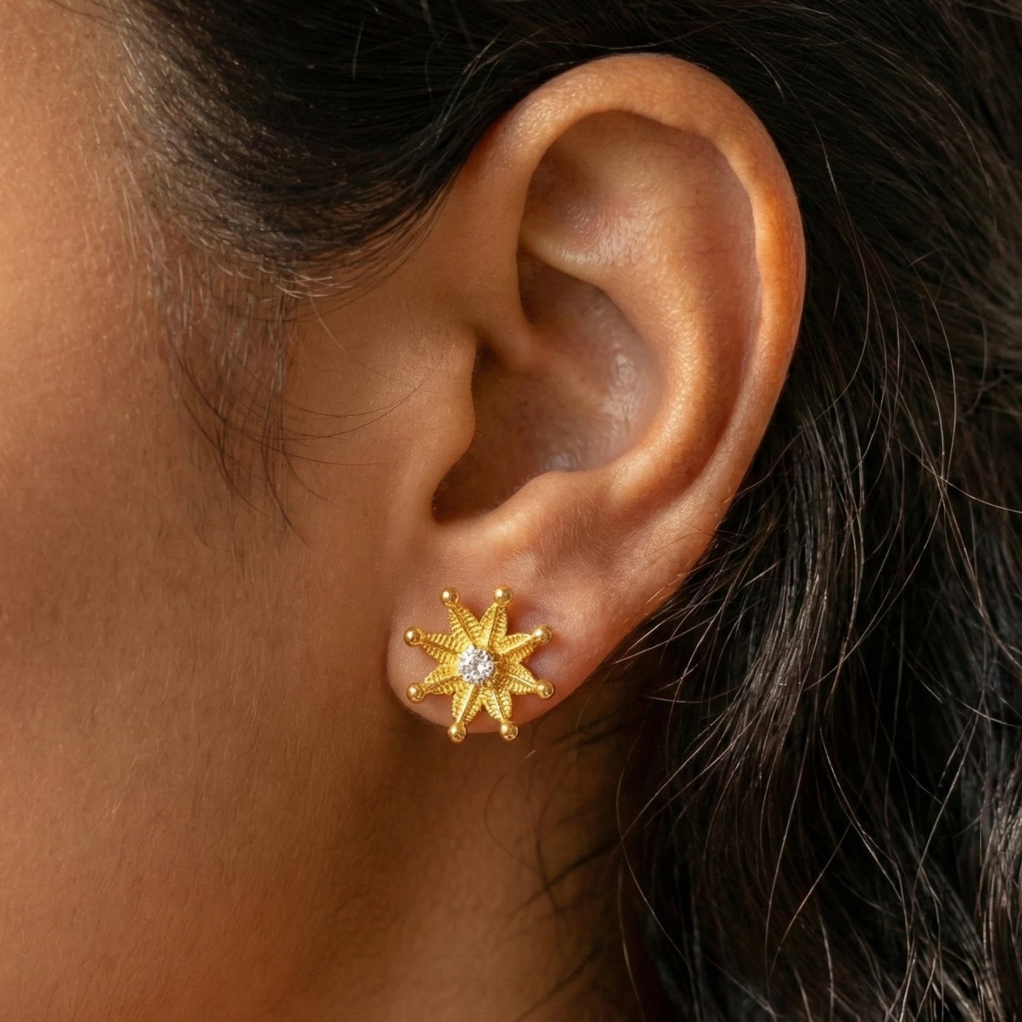 Gold plated star-shaped earring worn on an ear with dark hair.
