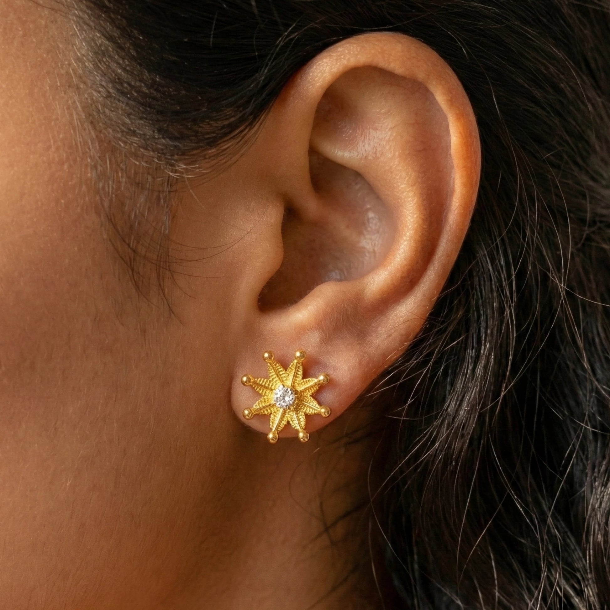 Gold plated star-shaped earring worn on an ear with dark hair.