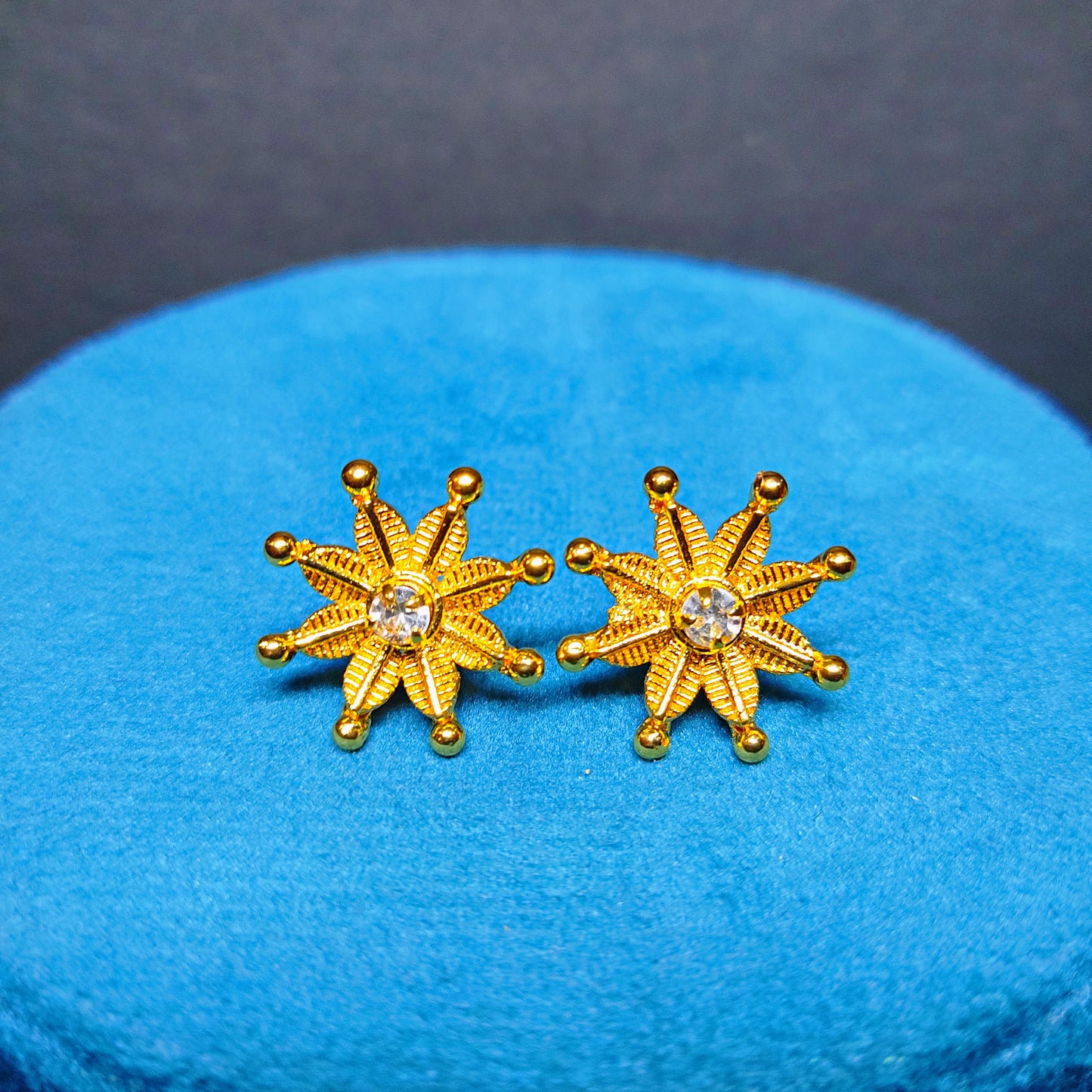 Gold Plated star-shaped earrings with a central gemstone on a blue cushion.