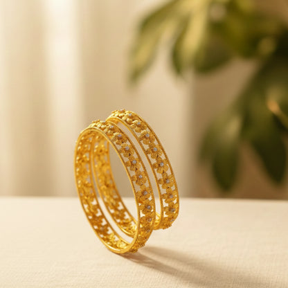 Gold plated bangles on a light surface with a blurred green plant in the background