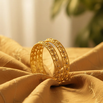 Gold plated bangles on a textured fabric surface with a blurred natural background