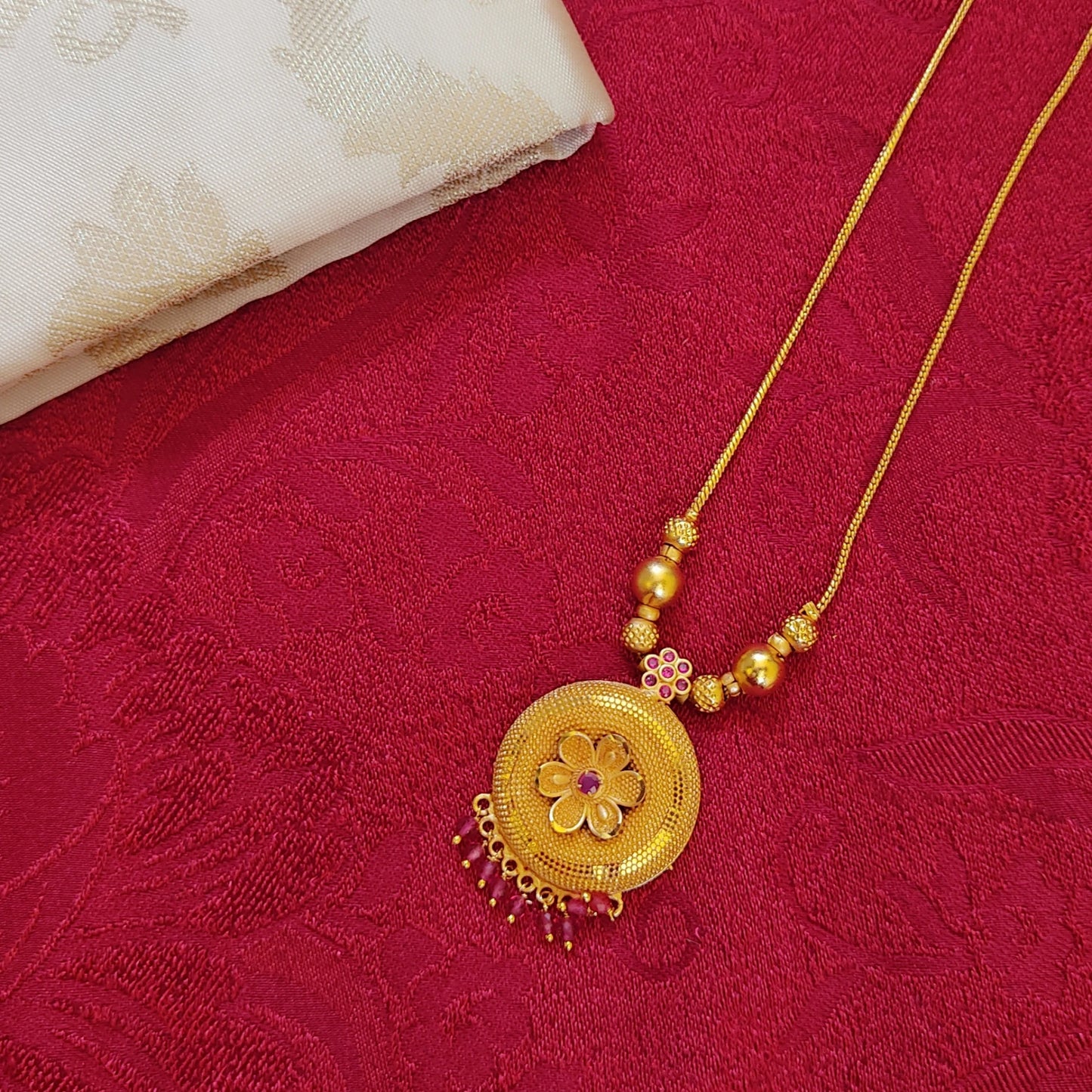 Gold plated necklace with floral pendant on a red fabric background