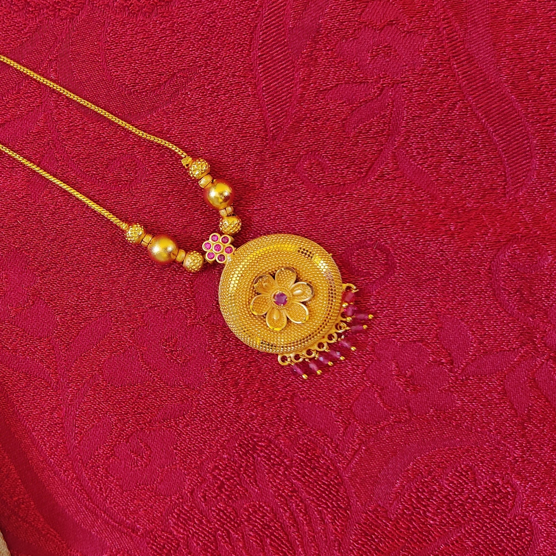 Gold plated necklace with a floral pendant on a red textured fabric background