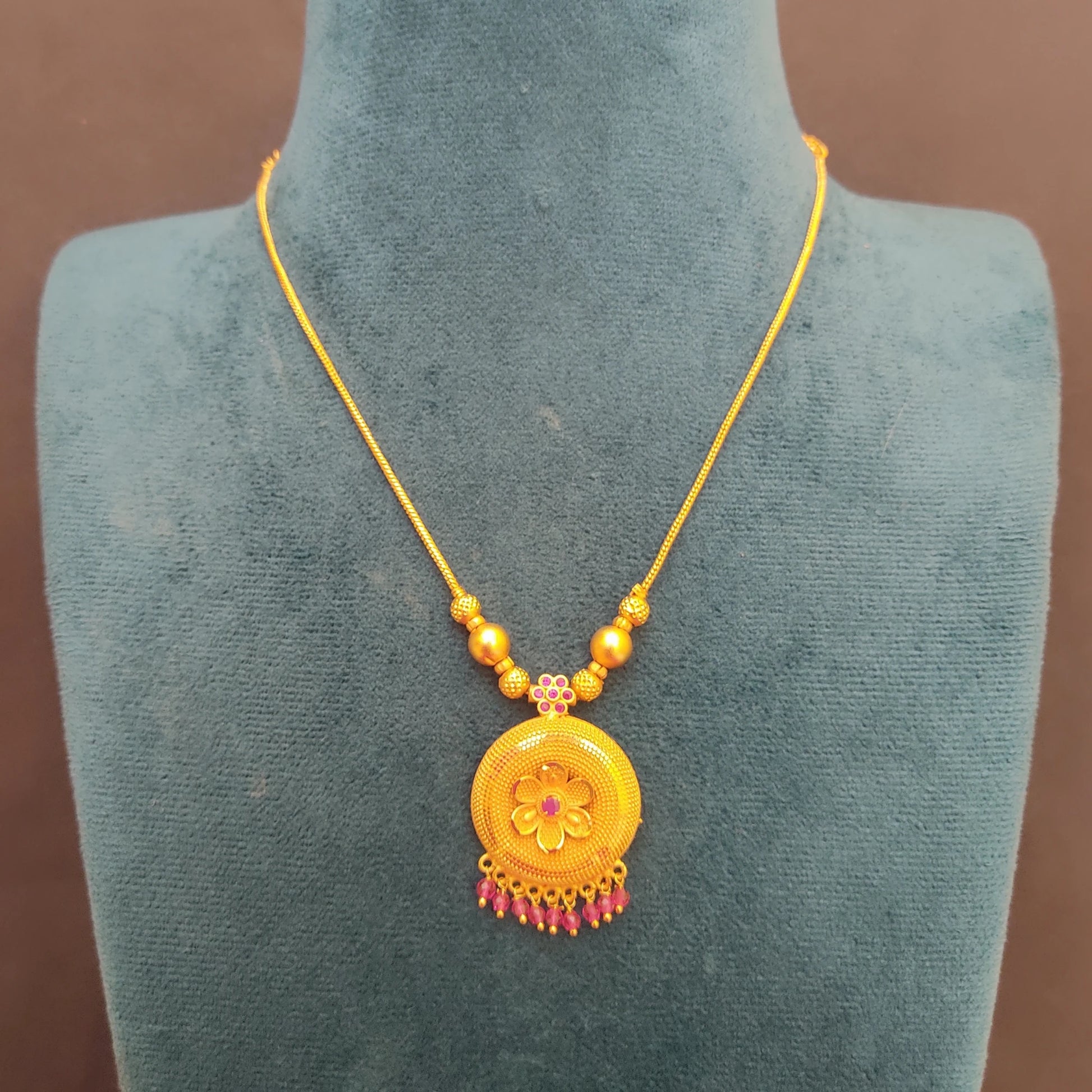 Gold Plated necklace with a floral pendant on a mannequin bust against a brown background