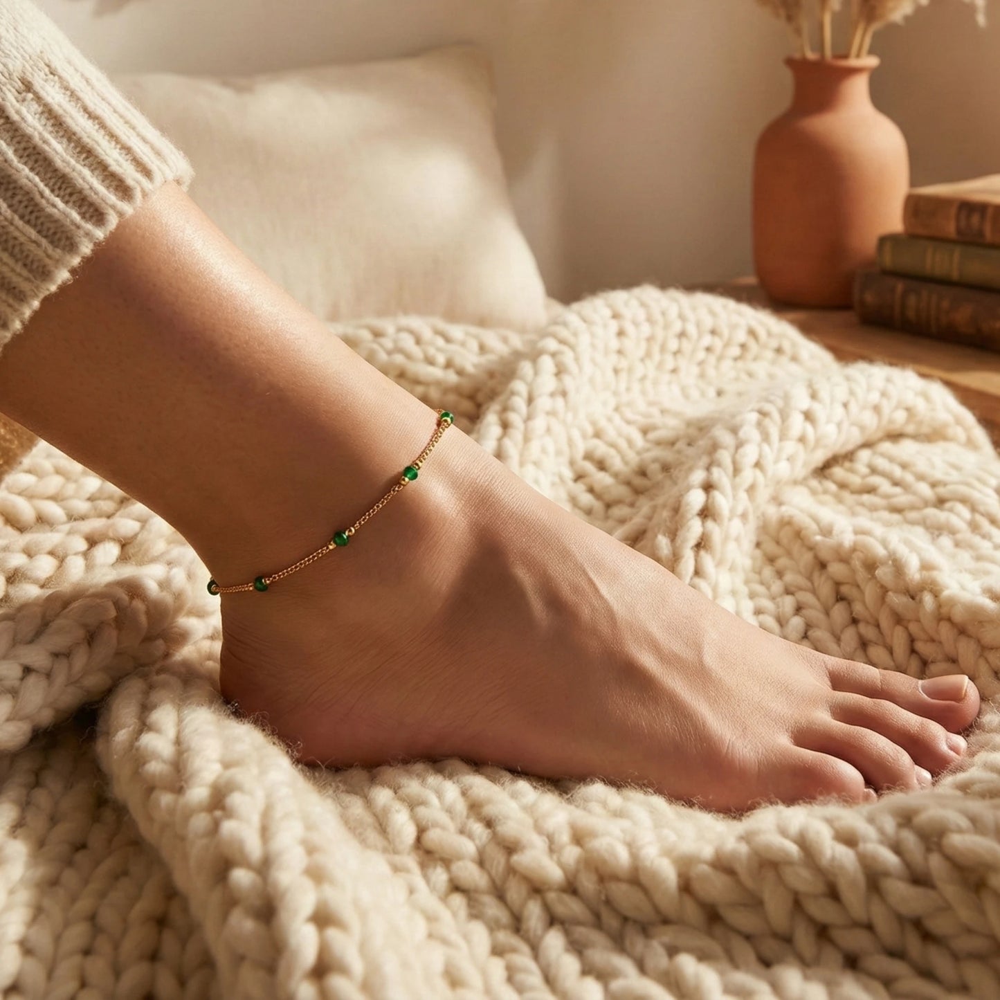 Person's foot with a gold plated anklet on a cozy blanket