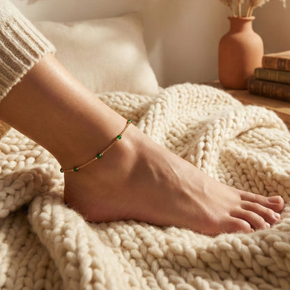 Person's foot with a gold plated anklet on a cozy blanket