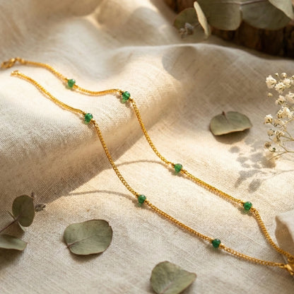 Gold plated Anklets with green beads on a textured fabric background