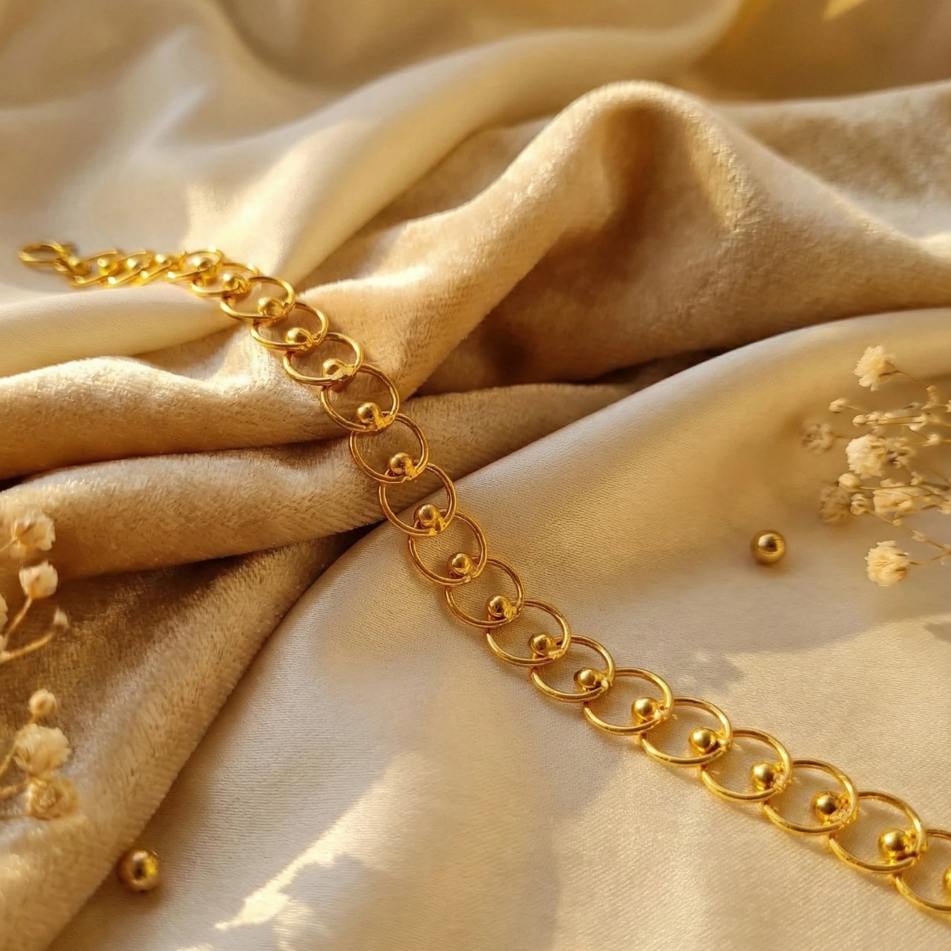 Gold plated chain bracelet on a beige fabric background with small flowers.