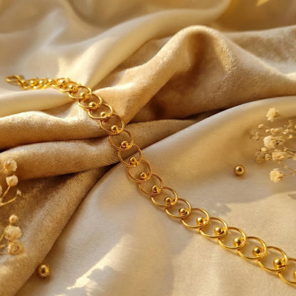 Gold plated chain bracelet on a beige fabric background with small flowers.