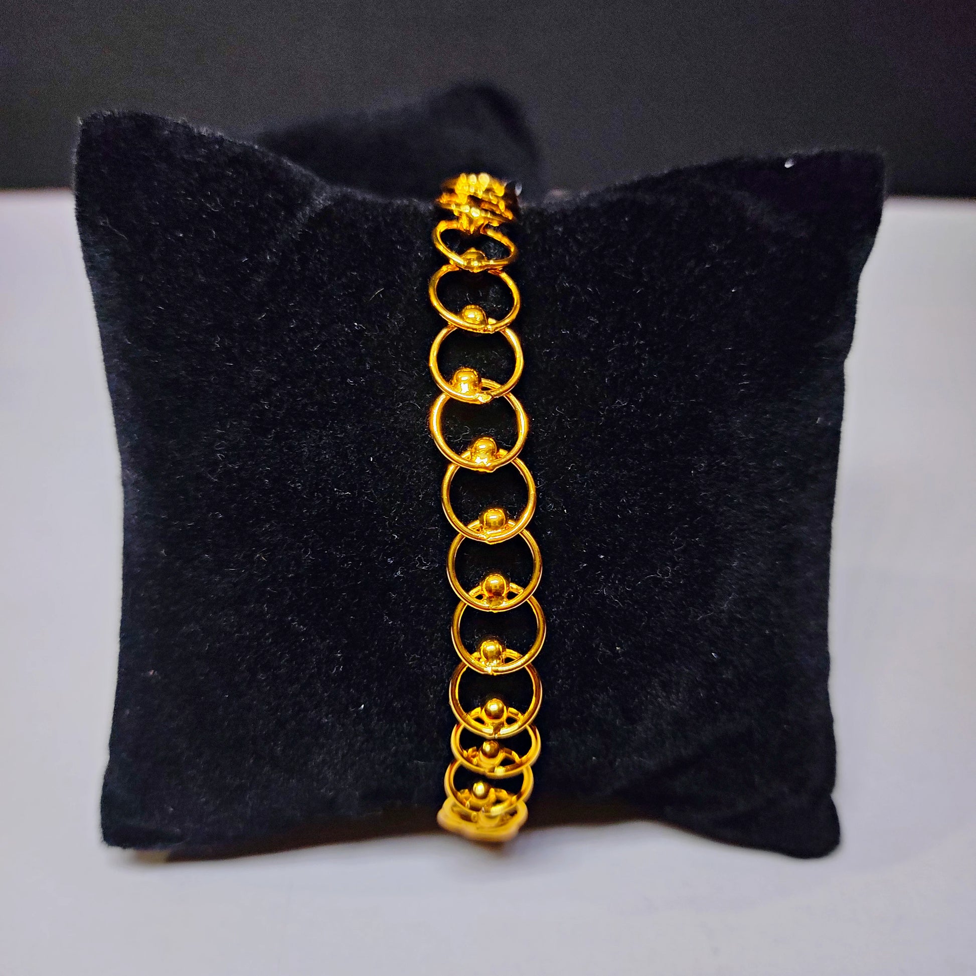 Gold plated bracelet on a black cushion with a gray background