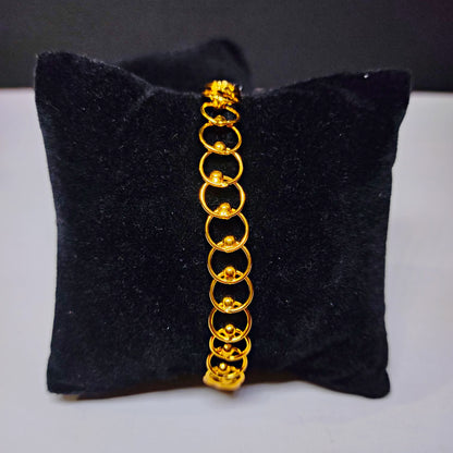 Gold plated bracelet on a black cushion with a gray background