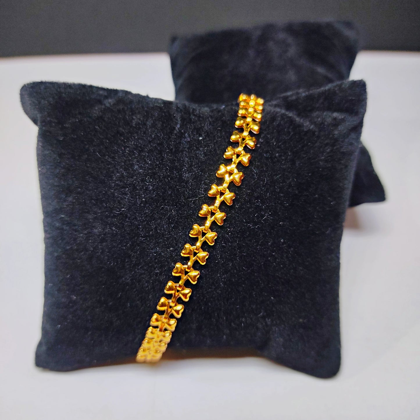 Gold plated bracelet on a dark gray cushion with a white background