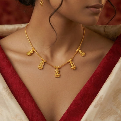 Gold plated necklace with Lakshmi pendant details worn by a person in a red and white saree.