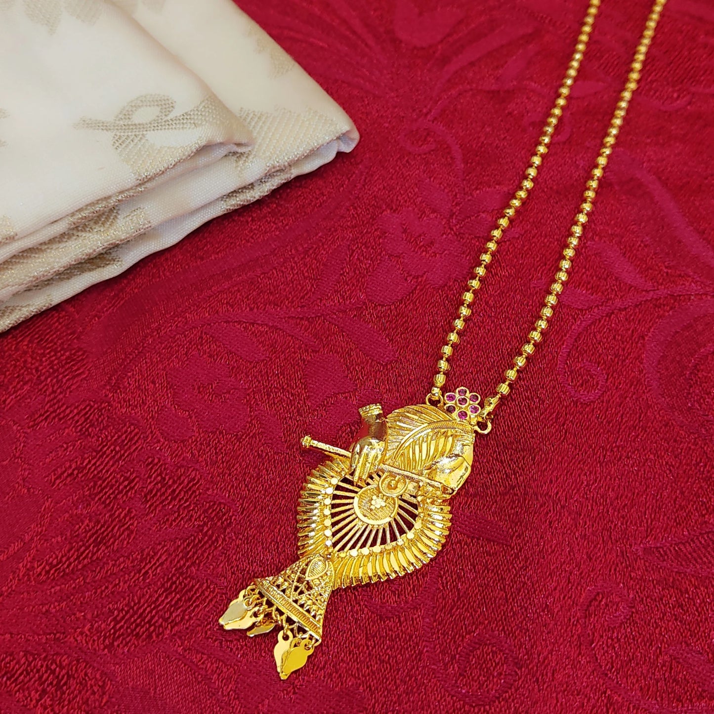 Gold plated necklace with a detailed Krishna with Flute pendant on a red fabric background