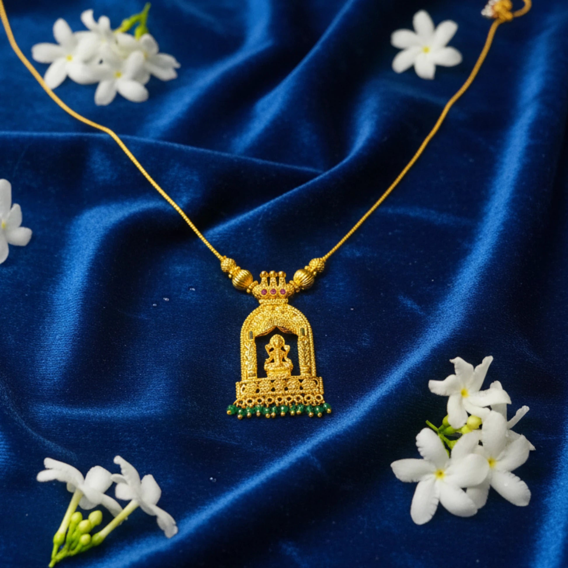 Gold plated necklace with Goddess Lakshmi in Temple Arch pendant on a blue fabric background with white flowers