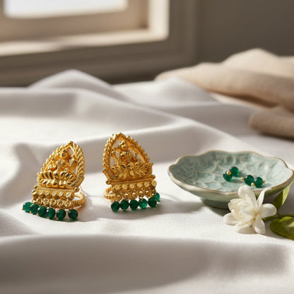 Gold plated earrings with lakshmi motif and  green beads on a white fabric background