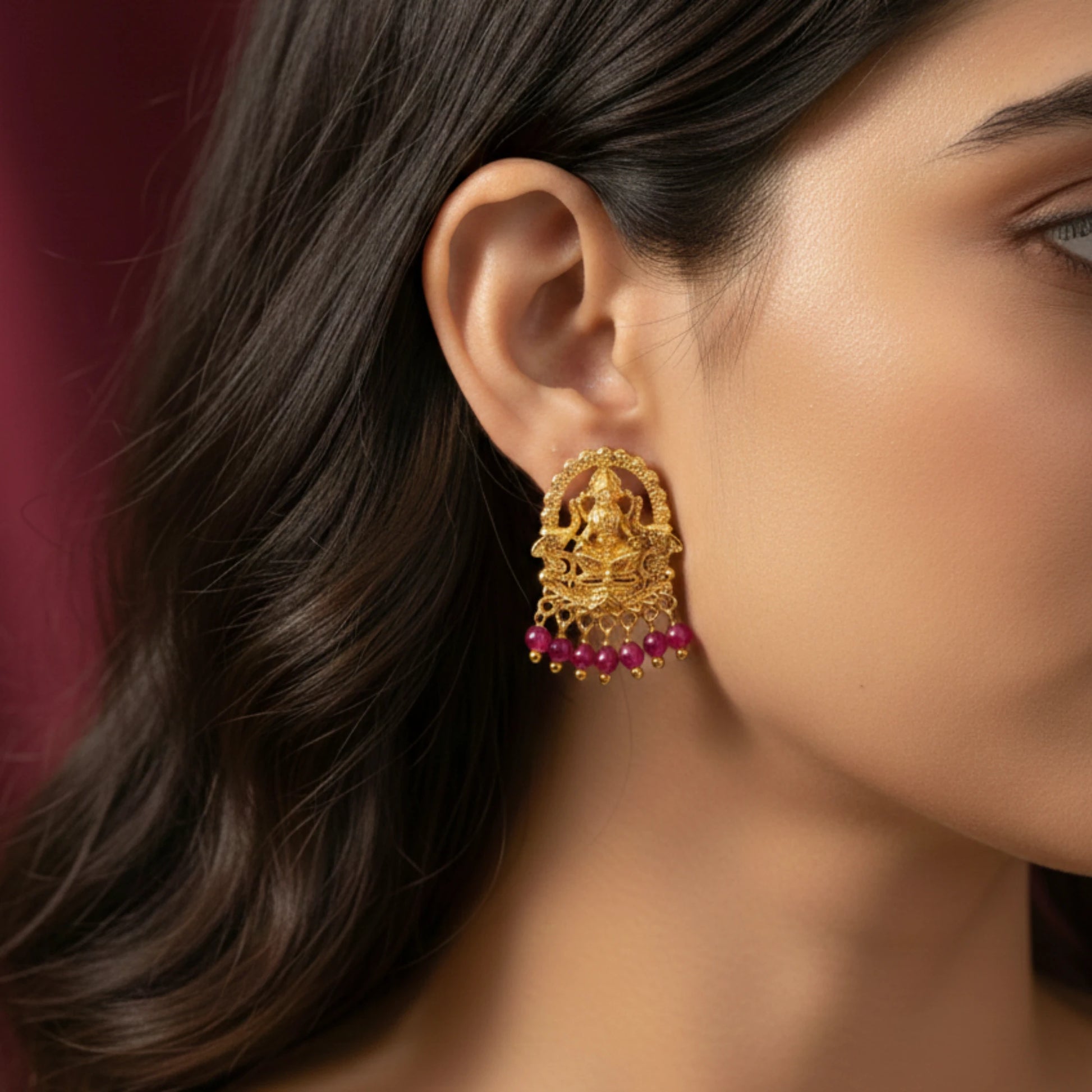 Close-up of a woman wearing gold plated lakshmi motif earrings with pink beads against a blurred background