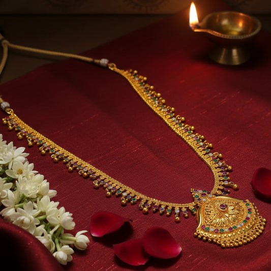 Gold Plated Long Haram necklace with colorful stones and a pendant on a red fabric background with flowers and a lit lamp.