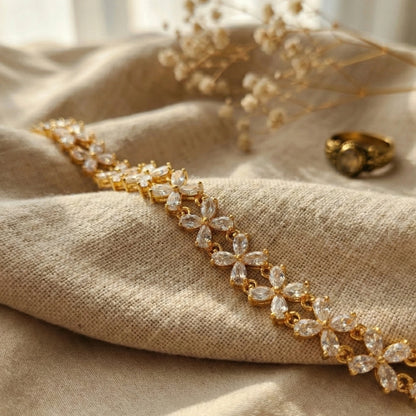 Gold plated bracelet with clear stones on beige fabric with dried flowers in the background