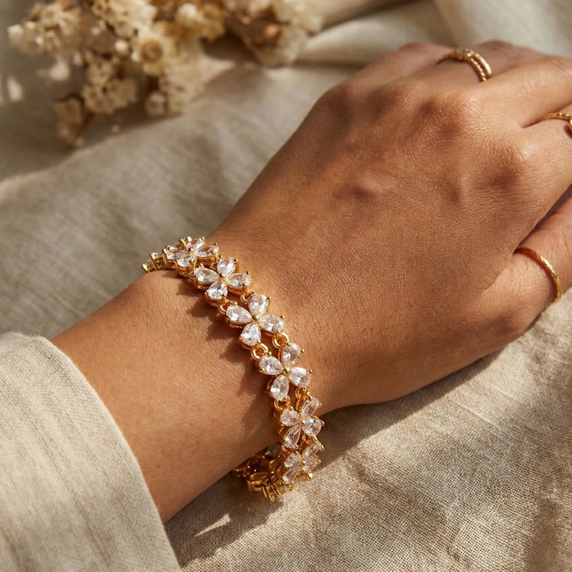 Hand wearing a gold plated bracelet with clear stones on a beige fabric background