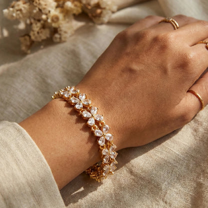 Hand wearing a gold plated bracelet with clear stones on a beige fabric background