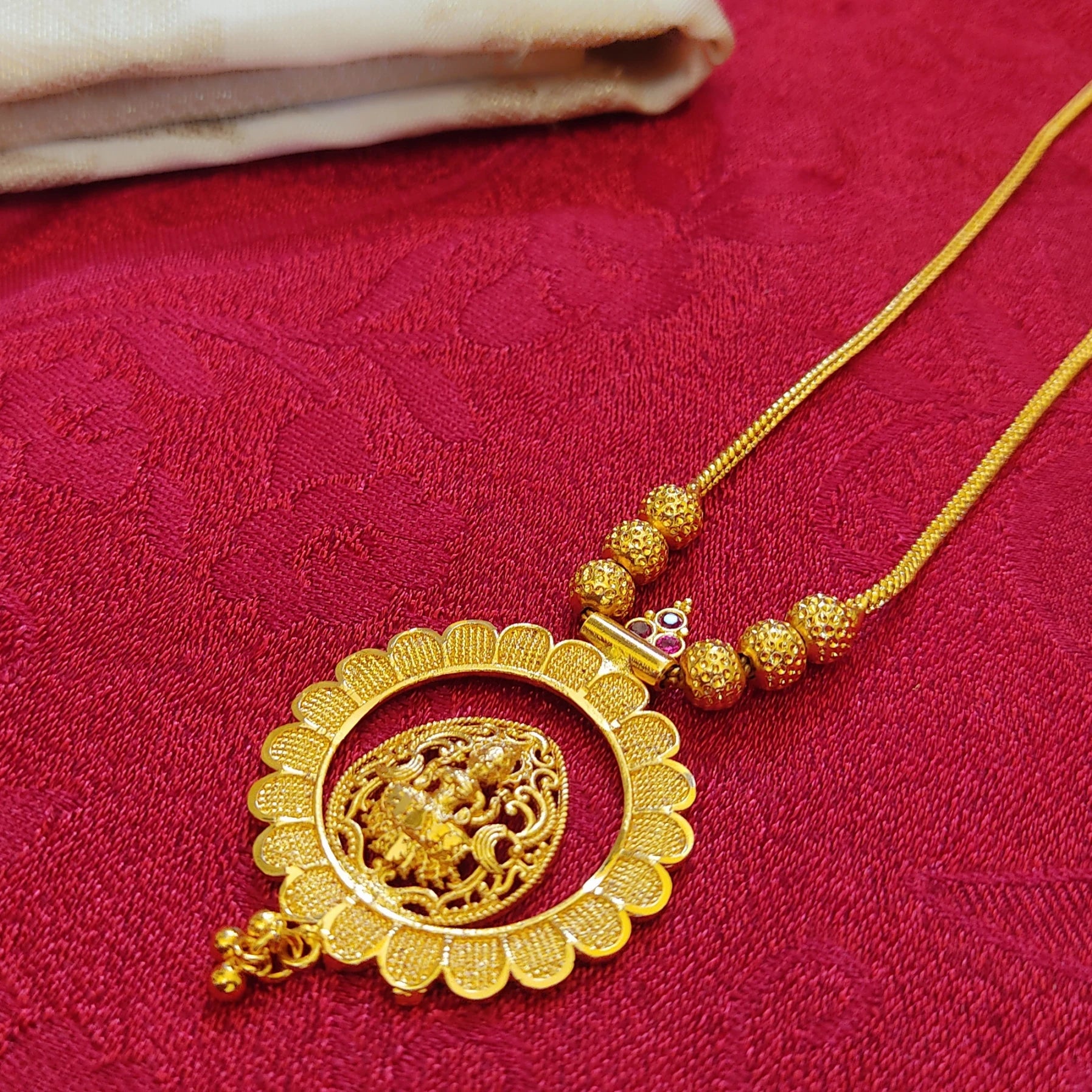 Gold plated necklace with intricate design and matte finish lakshmi on a lotus shaped central pendant on a red fabric background