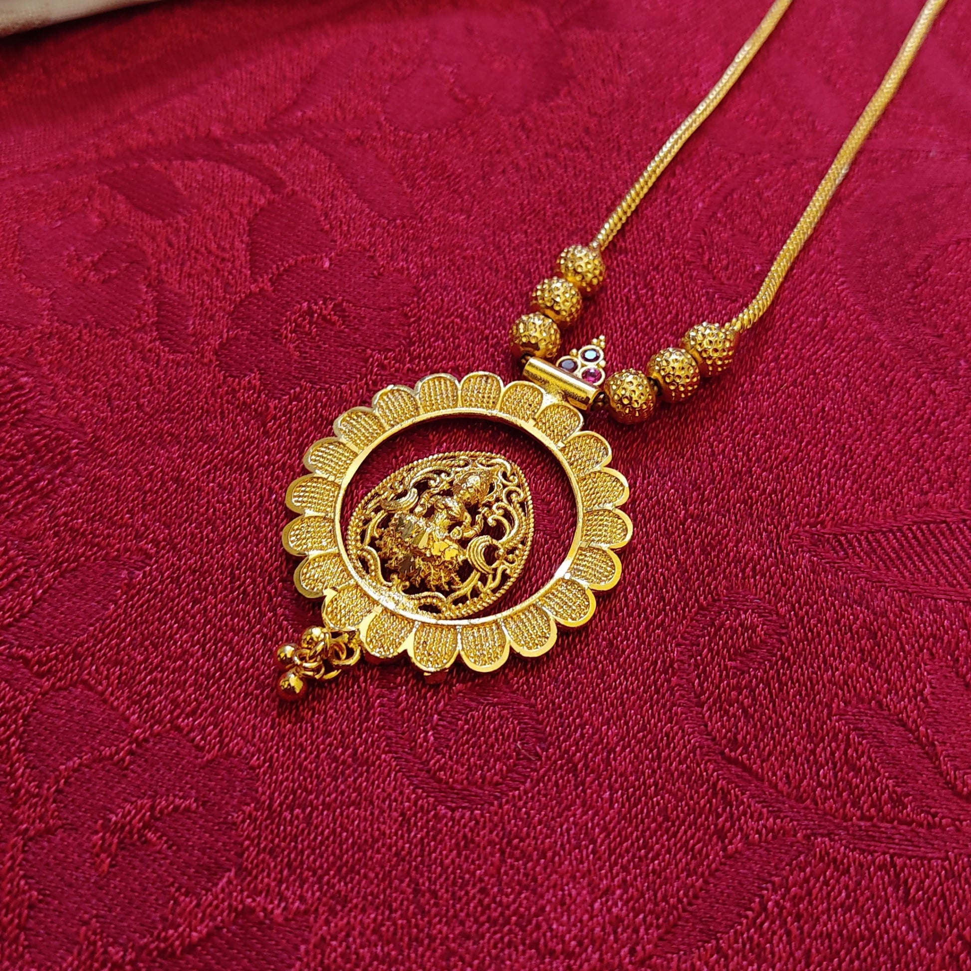 Gold plated necklace with intricate details in a lotus shaped pendant with Goddess Lakshmi on a red fabric background